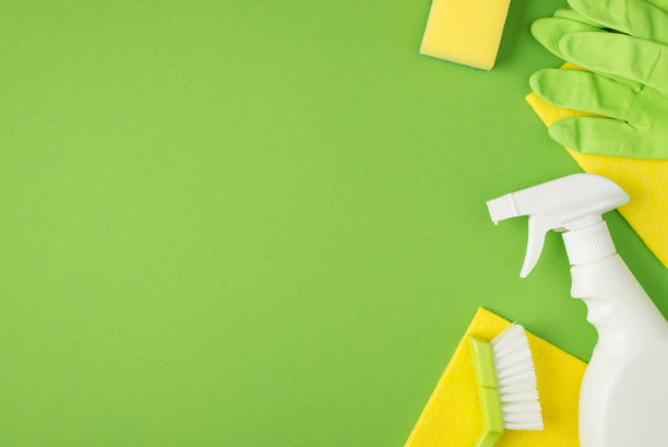 顶部视图照片洗涤剂喷雾瓶海绵刷黄色粘胶餐巾和绿色橡胶手套孤立的绿色背景与空白的左边图片下载