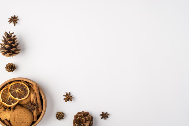 俯视图照片的冬季组成松果，八角和木碗饼干肉桂棒和干柠檬片在孤立的白色背景与copyspace图片下载