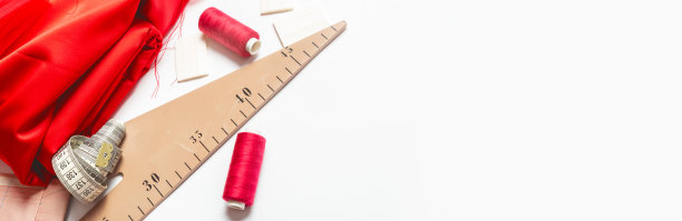 缝纫的概念。服装设计师工作。红色织物，线和剪刀在白色背景顶部视图空间的文本。横幅图片下载