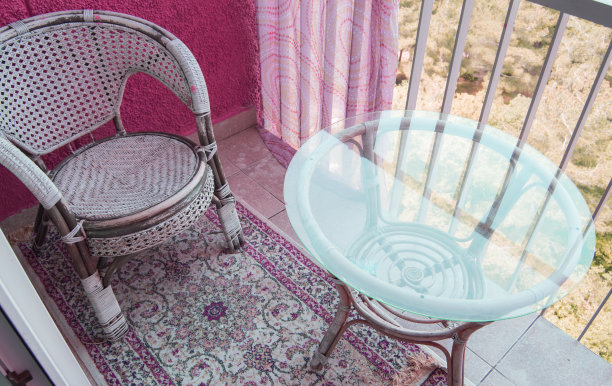 阳台上有一个舒适的座位区，有藤条柳条椅，透明的玻璃桌子和地毯，一个家庭娱乐的概念图片下载