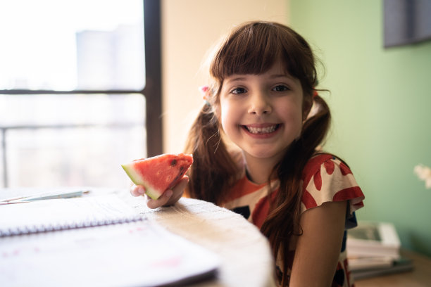 一个可爱的女孩在家里一边学习一边吃着西瓜片图片下载