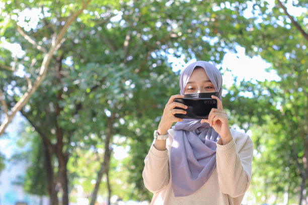 亚洲年轻女性在公园里用手机拍照片发到社交媒体上图片下载