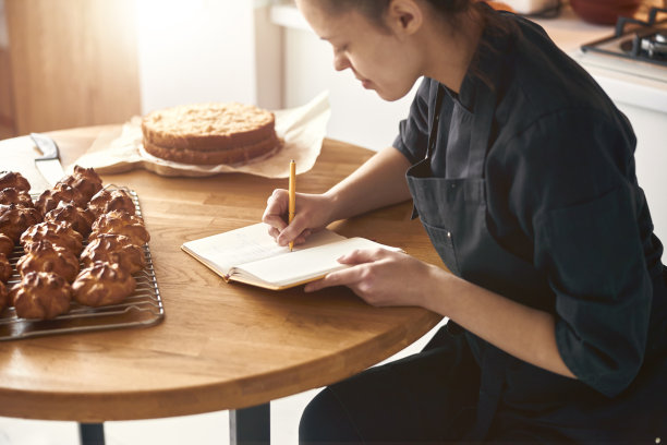 现代轻厨房的职业女厨师正在写泡芙的食谱图片下载