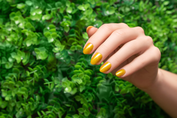 女性手与黄色指甲设计。亮黄色指甲油修指甲。女人手放在绿叶背景上。图片下载