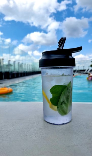 在清澈的蓝天下，泳池边的运动瓶里有柠檬、薄荷和冰图片下载