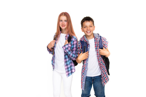 11岁的男生和女生背着书包，微笑着看着白色背景下的相机。穿着格子衬衫和白衬衫图片下载
