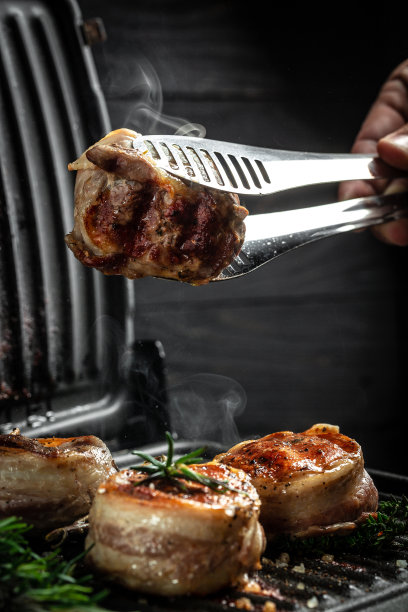 大奖章牛排从牛里脊覆盖培根烤架烟熏黑背景。厨师亲手烤制牛排图片下载