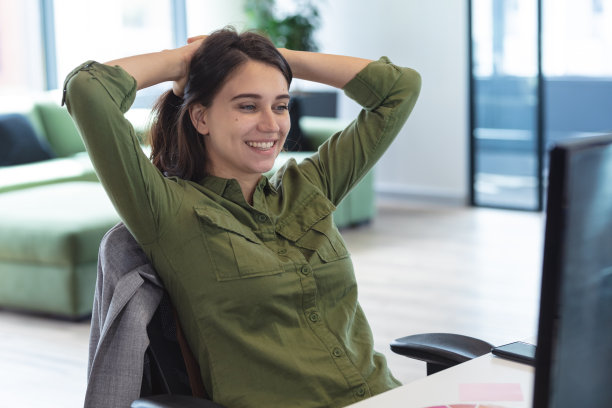 一名白人女性创意工作者，坐在办公桌前，面带微笑，举着头图片下载