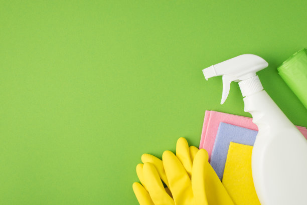 顶部视图照片的白色喷雾洗涤剂瓶子没有标签，多色粘胶布，垃圾袋和黄色橡胶手套孤立的绿色背景与copyspace图片下载