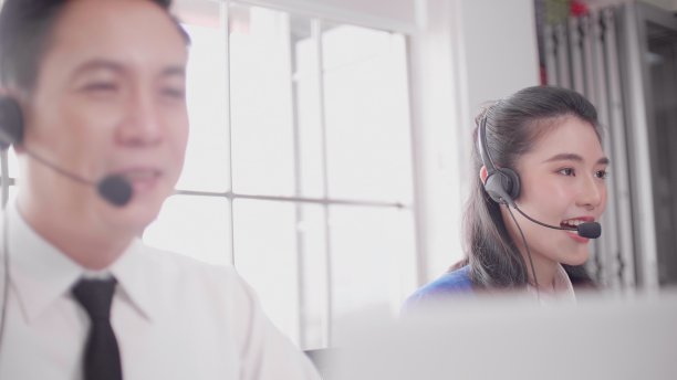 咨询和协助服务呼叫中心。年轻英俊的亚洲男性技术支持代理向客户解释一些事情。微笑的呼叫中心工作，通过耳机与客户交谈。图片下载