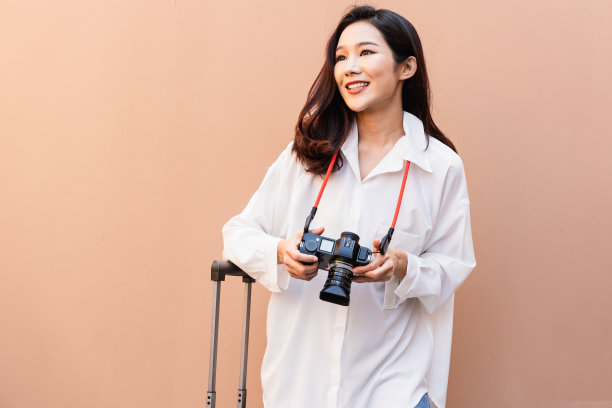 亚洲女性在夏日旅行时摆出时尚造型拍照。一个微笑的黑发女人的肖像，自然的化妆，穿着时尚的衣服。女旅行者拖着行李箱图片下载