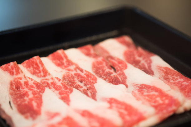 新鲜的切成薄片的牛肉放在黑色的托盘上，准备在餐厅涮涮锅。传统火锅的配料图片下载