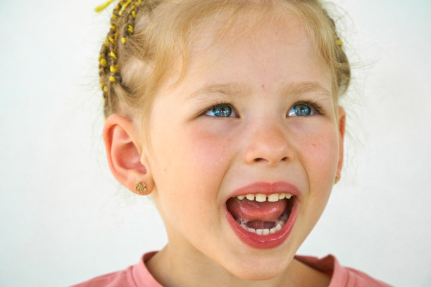 开朗的孩子。女孩笑特写的脸在白色的背景。一个小女孩露出了舌头和喉咙。张大嘴巴，伸出舌头的肖像。在视野清晰的情况下伸出长舌头图片下载