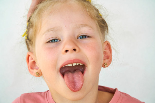 开朗的孩子。女孩笑特写的脸在白色的背景。一个小女孩露出了舌头和喉咙。张大嘴巴，伸出舌头的肖像。在视野清晰的情况下伸出长舌头图片下载