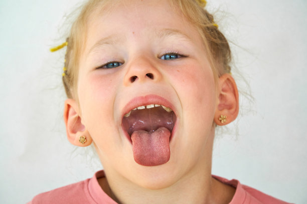 开朗的孩子。女孩笑特写的脸在白色的背景。一个小女孩露出了舌头和喉咙。张大嘴巴，伸出舌头的肖像。在视野清晰的情况下伸出长舌头图片下载