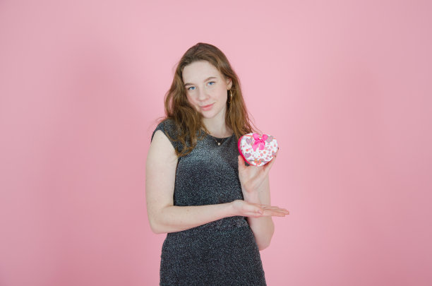 女孩手里拿着一份礼物，背景是粉红色的。情人节、圣诞节、儿童节、妇女节图片下载