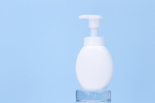 无品牌的白色瓶子与泵在玻璃讲台和大白色鸵鸟羽毛在蓝色背景。防晒霜。空白标签瓶的品牌。化妆品包装模型。图片下载