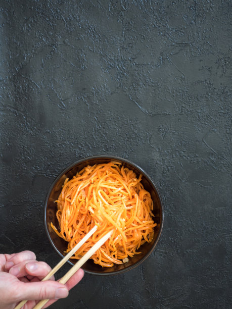 男人的手用筷子夹着胡萝卜吃韩国沙拉。平的。垂直图片下载