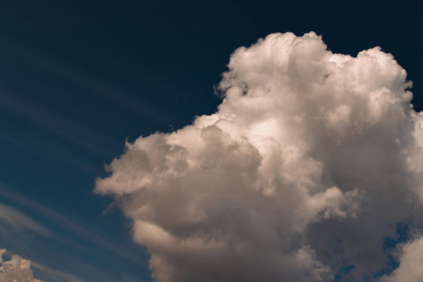 图片右侧的白色积云，被灰色的阴影遮住，漂浮在蓝色天空中的薄云幕下。图片下载