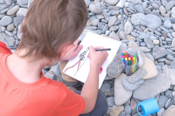 男孩坐在海边的石滩上用马克笔画画图片下载