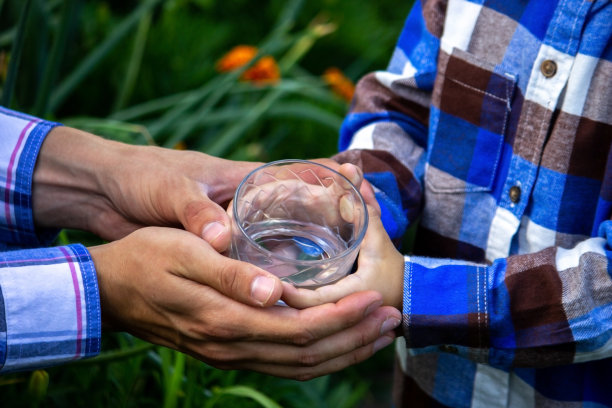 孩子和父亲手中的玻璃杯中的水。自然。图片下载