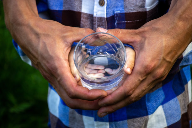 孩子和父亲手中的玻璃杯中的水。自然。图片下载