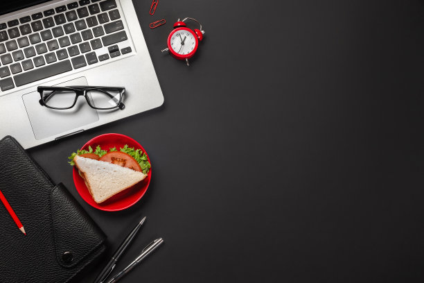优雅的黑色办公桌面，配有笔记本电脑，一杯咖啡和一个三明治作为午餐。俯视图图片下载