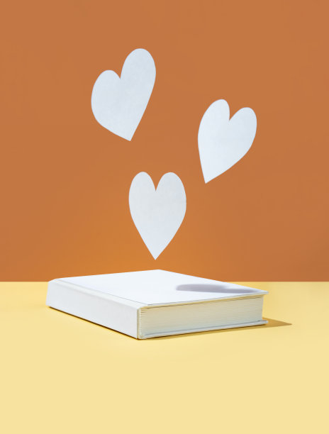 浮动可爱的纸心和白色封面书的颜色大胆的黄色和橙棕色的背景。现代的照片。概念国家图书爱好者日。宗教节日快乐。浪漫,爱讲故事。本空间图片下载