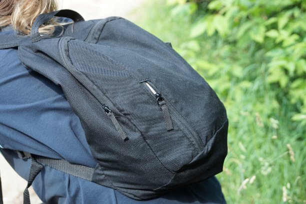 在街上，一个穿着蓝色衬衫的旅游女孩背着一个黑色的织物背包图片下载