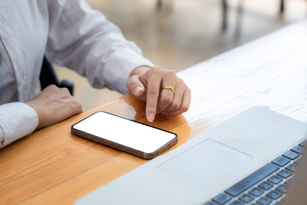 特写的女商人手与智能手机白屏和笔记本电脑键盘放在办公室。图片下载