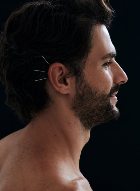 英俊男子有耳针治疗疾病，黑色背景，侧面视图。针灸，反射学，中医图片下载
