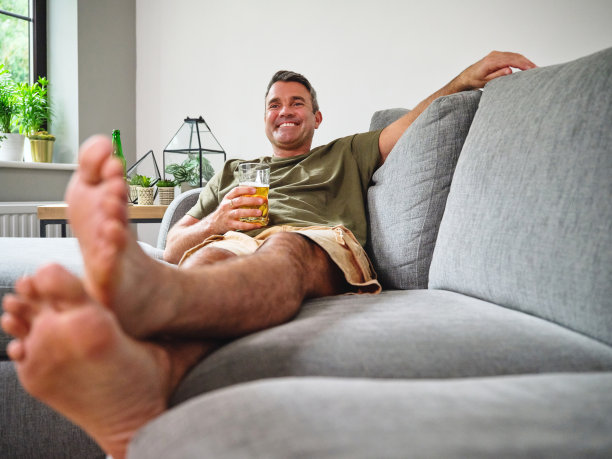 一个成熟的男人在家里的沙发上喝着啤酒图片下载