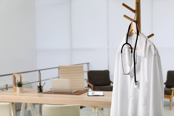 现代化的医生工作场所，木桌，白大褂挂在办公室的架子上图片下载