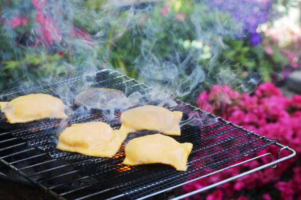 图片的前景是吸烟的便携式，在花园里的木炭烧烤，在户外的金属烤架上烹饪的汉堡，在汉堡肉饼上融化的加工奶酪片图片下载