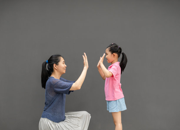母亲和女儿在灰色背景下击掌图片下载