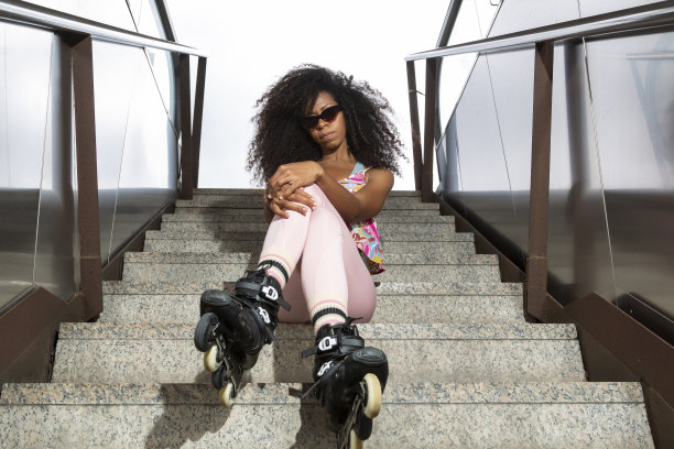 黑色女滑板手戴着太阳镜，坐在楼梯上看着摄像机图片下载