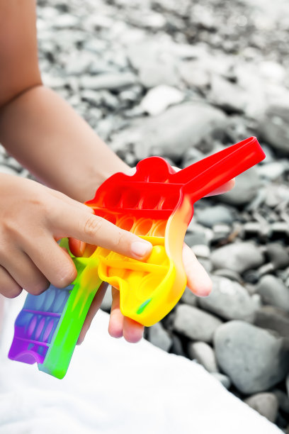 一个孩子在白色毛巾布的背景下，在海卵石滩上玩着一个五颜六色的独角兽形状的泡泡。Popit在一个孩子手里。图片下载