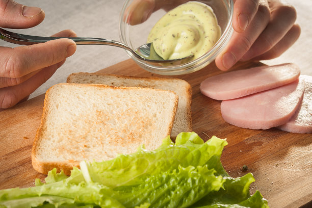 双手放在木制砧板上，用面包、奶酪、沙拉和火腿制作三明治图片下载