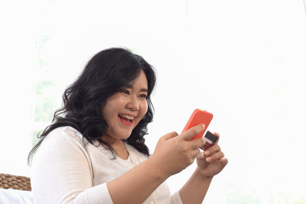 胖或大女人坐在藤椅上使用红色手机网上购物和信用卡支付。图片下载