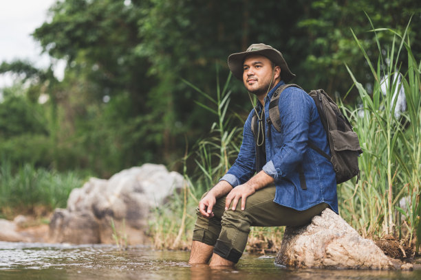 徒步旅行者在山间的河边休息。背着背包的徒步旅行者在山上触摸淡水。快乐自由的概念。图片下载