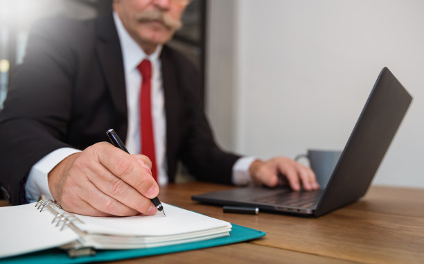靠近资深商人手里拿着黑色的笔和电脑签纸。资深人士在办公室写组织者。商业教育知识概念图片下载