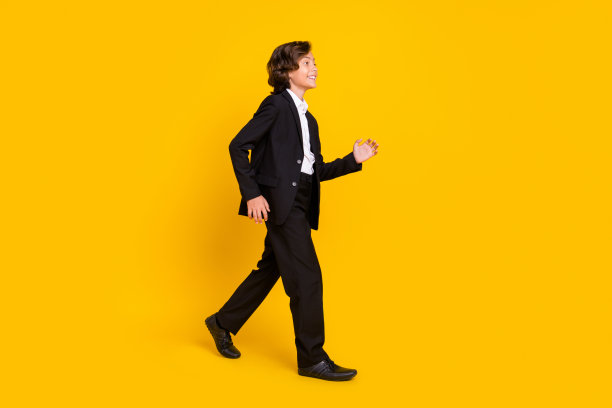 正面小男孩侧面照片，享受散步穿着黑色制服鞋孤立黄色背景图片下载