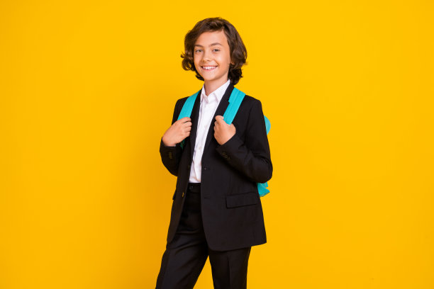开朗积极的小男生的照片，背包黑色制服孤立的黄色背景图片下载