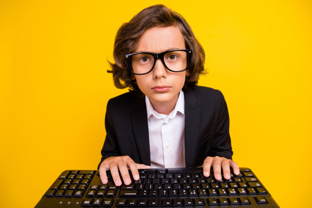 图片冷静的学习男孩打字键盘看网络相机戴眼镜黑色统一孤立黄色背景图片下载