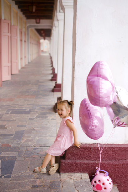 一个女孩拿着气球和一个装着动物的篮子站在柱子旁边图片下载