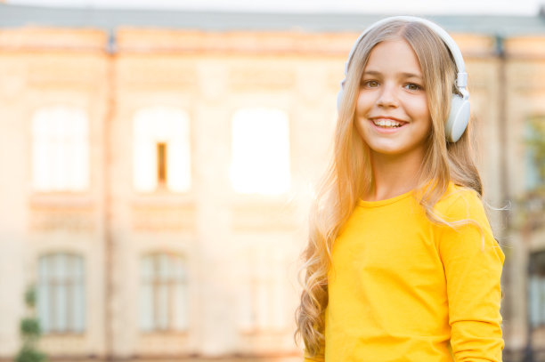 音乐频道。使用现代科技的孩子。音乐的灵魂。现代的孩子。女孩听音乐的现代小玩意。孩子快乐的无线耳机户外日落城市背景。立体声耳机图片下载