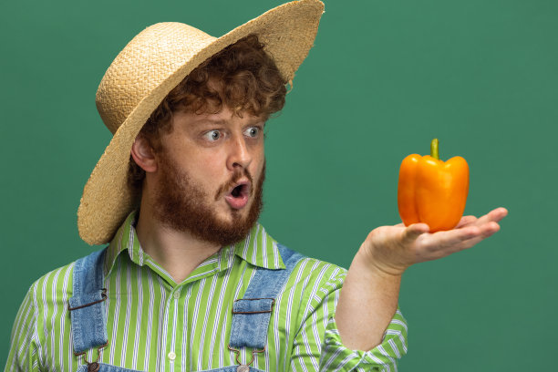 特写有趣的红发大胡子男子，农民与黄胡椒孤立地站在绿色的工作室背景。职业、工作的概念。图片下载