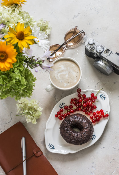 美味的早午餐-甜甜圈与巧克力糖霜，卡布奇诺，鲜花，相机，计划在一个轻的石头背景，俯视图图片下载