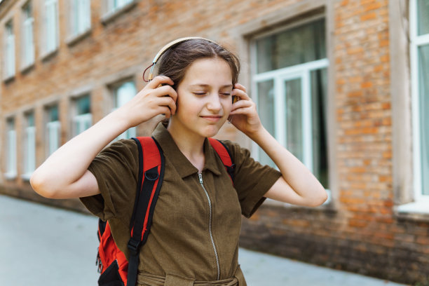 快乐的女学生在上学的路上。她戴着耳机听音乐。教育和返校观念图片下载