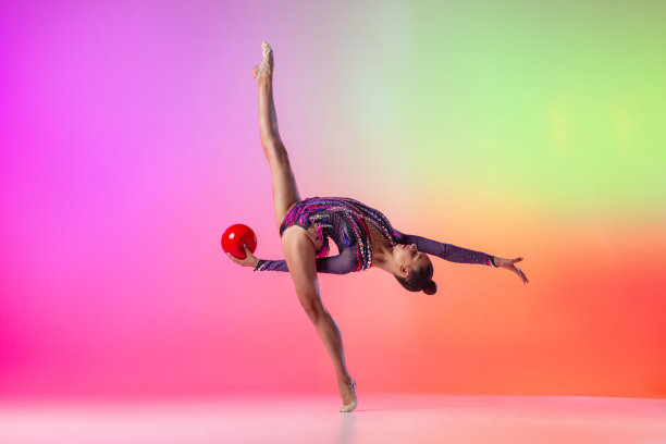 年轻的女孩，艺术体操运动员与红色的球在运动和行动孤立的彩色霓虹灯背景。图片下载